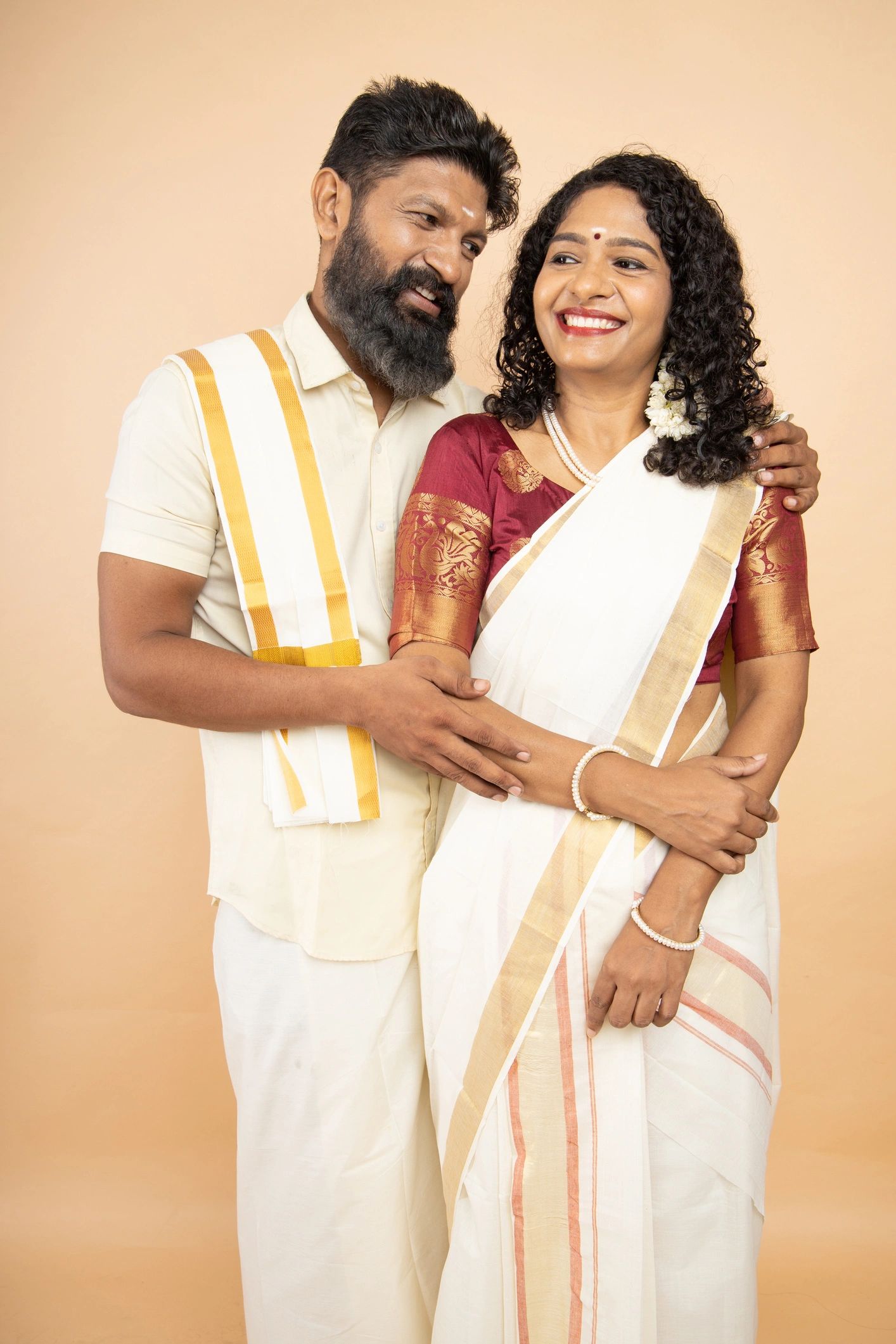 Portrait of happy south indian couple wearing traditional white dress isolated on beige background